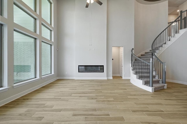 216 Ranchland Pass, Liberty Hill, TX 78642 - unfurnished living room featuring a towering ceiling, light wood-style floors, stairs, ceiling fan, and a glass covered fireplace