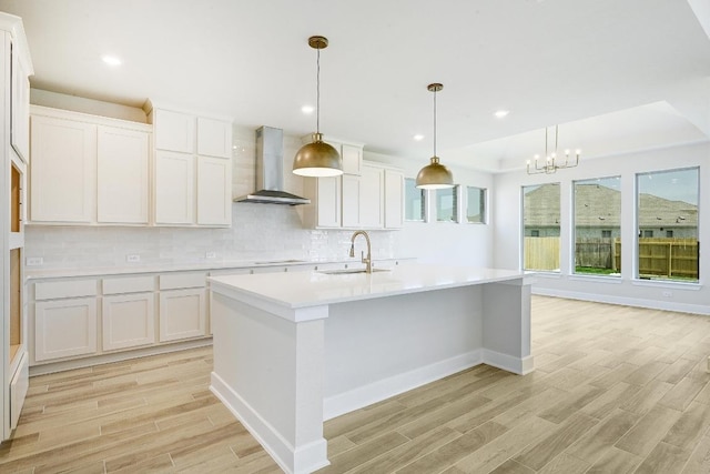 216 Ranchland Pass, Liberty Hill, TX 78642 - kitchen featuring wall chimney exhaust hood, light wood-style flooring, light countertops, tasteful backsplash, and a kitchen island with sink