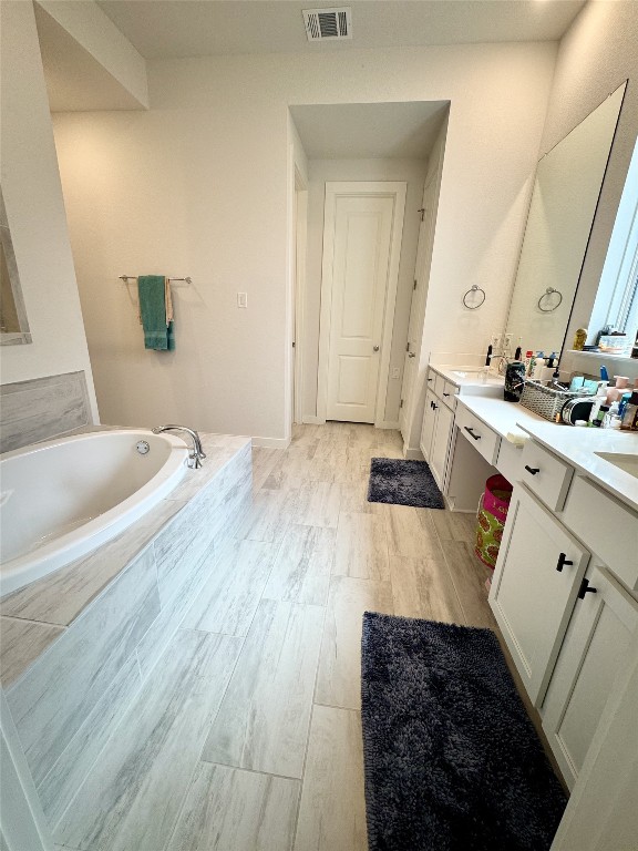 422 Billowing Way, Kyle, TX 78640 - bathroom featuring double vanity, a garden tub, and wood finished floors