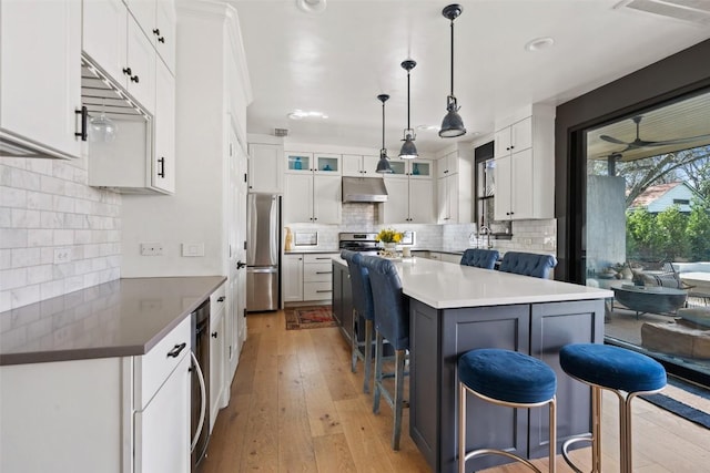 1102 Kinney Ave, Austin, TX 78704 - kitchen with under cabinet range hood, stainless steel appliances, a kitchen breakfast bar, tasteful backsplash, and light wood-type flooring