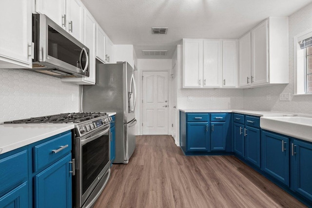 11220 Amaranth Ln, Austin, TX 78754 - kitchen with appliances with stainless steel finishes, blue cabinets, wood finished floors, and white cabinets