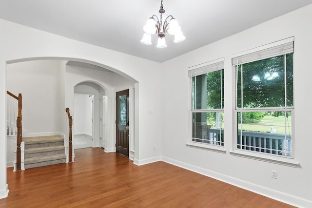 221 Mcgarity St, Kyle, TX 78640 - spare room with a chandelier, wood finished floors, stairs, baseboards, and arched walkways