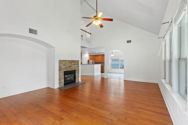 221 Mcgarity St, Kyle, TX 78640 - unfurnished living room featuring a ceiling fan, arched walkways, high vaulted ceiling, light wood finished floors, and a stone fireplace