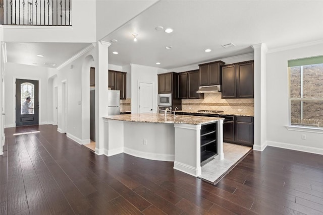 8508 Lookout Cliff Pass, Austin, TX 78737 - kitchen featuring appliances with stainless steel finishes, under cabinet range hood, dark brown cabinetry, light stone countertops, and decorative backsplash