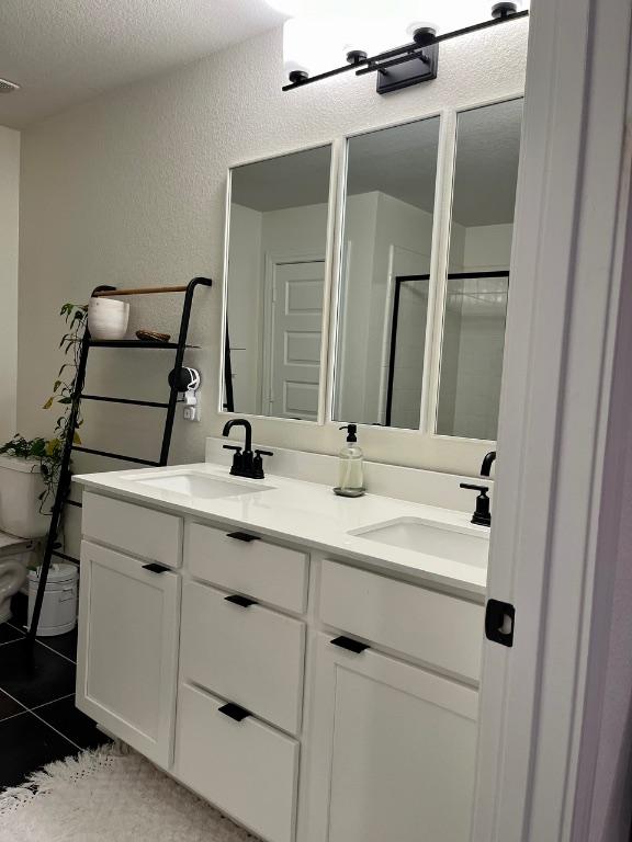 14217 Silver Lace Ln, Pflugerville, TX 78660 - full bathroom with a textured wall, double vanity, a textured ceiling, a shower with door, and tile patterned floors