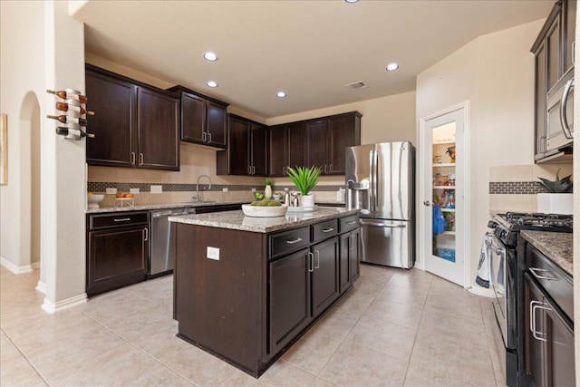 1366 Red Stag Pl, Round Rock, TX 78665 - kitchen with stainless steel appliances, dark brown cabinetry, backsplash, a center island, and light stone countertops
