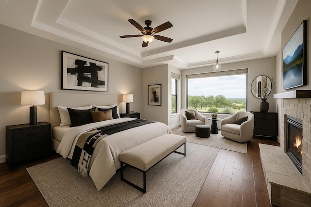144 Serene St, Spring Branch, TX 78070 - bedroom featuring a tray ceiling, a tiled fireplace, dark wood-style flooring, a ceiling fan, and ornamental molding