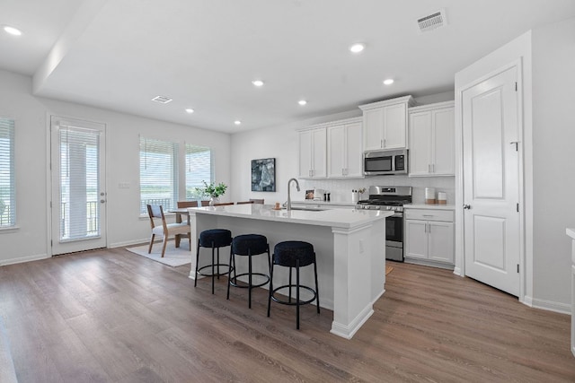 529 Leeward Pass, Leander, TX 78641 - kitchen with appliances with stainless steel finishes, a center island with sink, wood finished floors, a kitchen breakfast bar, and white cabinetry