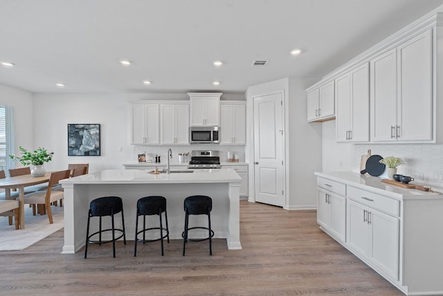 529 Leeward Pass, Leander, TX 78641 - kitchen with stainless steel appliances, white cabinets, a kitchen bar, light wood-type flooring, and recessed lighting