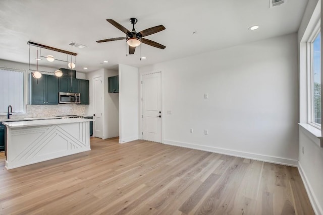 4127 E 12th St Unit 5, Austin, TX 78721 - kitchen with stainless steel microwave, decorative backsplash, ceiling fan, light wood finished floors, and light countertops