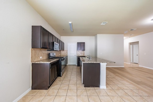 1605 Atlas Rd, Cedar Park, TX 78613 - kitchen with stainless steel appliances, decorative backsplash, dark brown cabinetry, a center island with sink, and light stone countertops