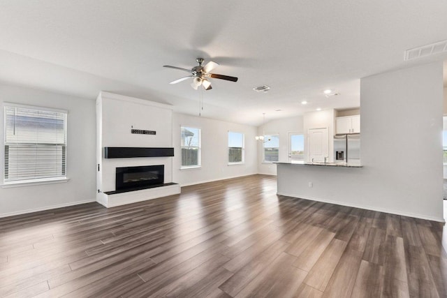 133 Nathaniel Dr, Taylor, TX 76574 - unfurnished living room with dark wood-style flooring, a ceiling fan, a glass covered fireplace, a chandelier, and recessed lighting