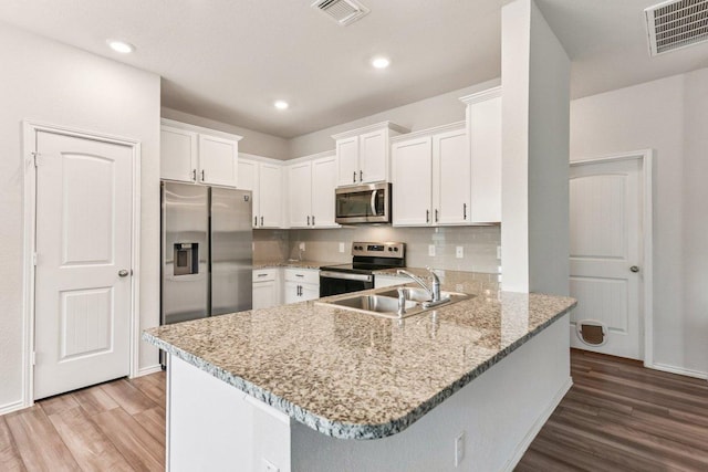 133 Nathaniel Dr, Taylor, TX 76574 - kitchen with stainless steel appliances, wood finished floors, a peninsula, white cabinets, and light stone countertops