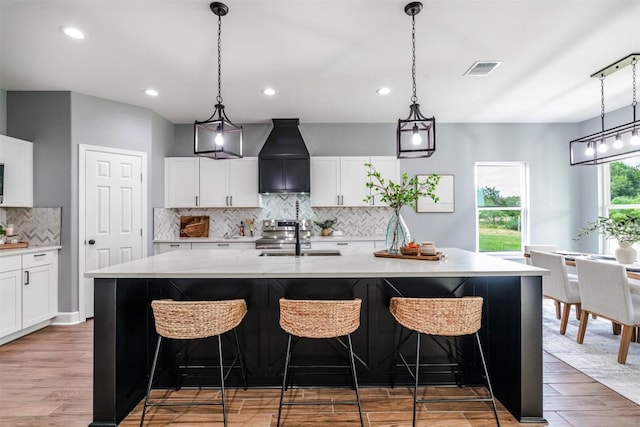 367 Stockade Ranch Rd, Paige, TX 78659 - kitchen featuring premium range hood, a sink, backsplash, light wood-style floors, and a kitchen island with sink