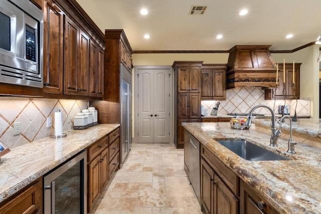 104 Porto Cima Ct, Austin, TX 78738 - kitchen featuring appliances with stainless steel finishes, wine cooler, custom range hood, crown molding, and light stone counters
