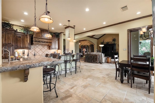 104 Porto Cima Ct, Austin, TX 78738 - kitchen with arched walkways, a breakfast bar area, stone tile flooring, dark brown cabinetry, and tasteful backsplash