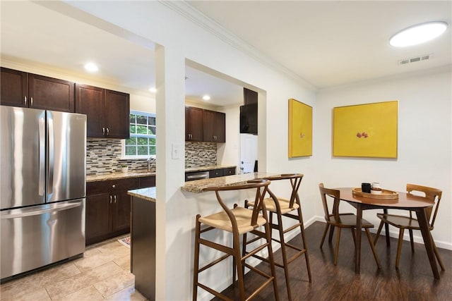 605 Orland Blvd, Austin, TX 78745 - kitchen featuring appliances with stainless steel finishes, a breakfast bar, crown molding, tasteful backsplash, and dark brown cabinetry
