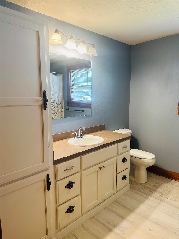 486 E Galveston St, Giddings, TX 78942 - bathroom featuring wood finished floors, vanity, toilet, and a textured ceiling
