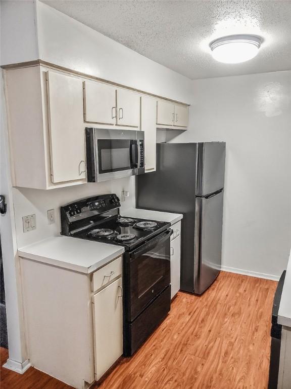 106 E 30th St Unit 305, Austin, TX 78705 - kitchen featuring appliances with stainless steel finishes, a textured ceiling, light wood-style flooring, light countertops, and white cabinets