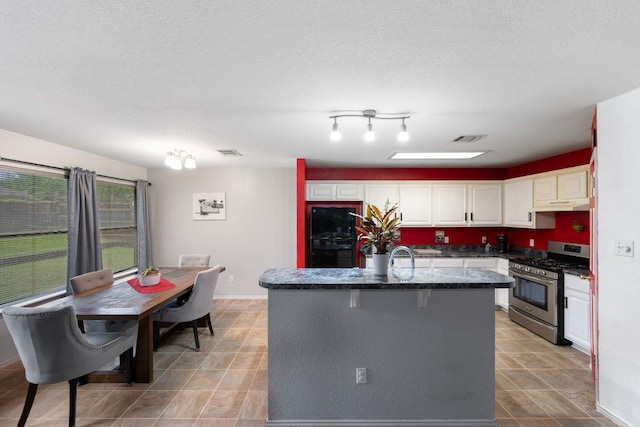 1207 Rolling Ridge Dr, Round Rock, TX 78665 - kitchen featuring stainless steel gas range, white cabinets, under cabinet range hood, an island with sink, and dark stone countertops