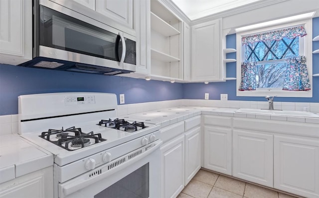762 S Guadalupe St, Lockhart, TX 78644 - kitchen with white gas stove, open shelves, stainless steel microwave, tile counters, and a sink