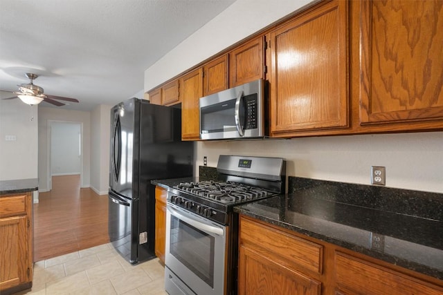 8407 Bargamin Dr, Austin, TX 78736 - kitchen featuring stainless steel appliances, brown cabinetry, ceiling fan, dark stone counters, and light tile patterned floors