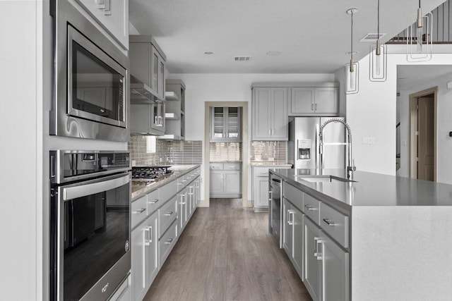 8108 Turning Leaf Cir, Lago Vista, TX 78645 - kitchen featuring appliances with stainless steel finishes, a sink, gray cabinetry, backsplash, and wood finished floors