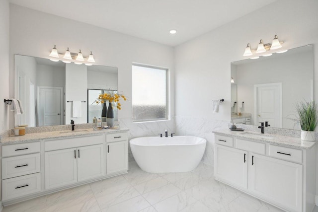 2436 Capestrano Cir, Round Rock, TX 78665 - bathroom featuring marble look tiles, two vanities, a freestanding bath, a wainscoted wall, and tile walls