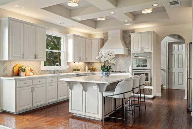 512 Newhall Cv, Austin, TX 78746 - kitchen featuring custom range hood, coffered ceiling, a kitchen bar, white cabinets, and dark wood finished floors