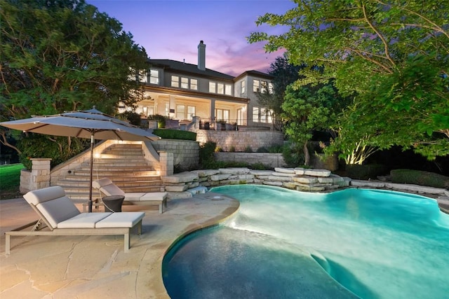 512 Newhall Cv, Austin, TX 78746 - back of property at dusk with stairway, a patio, an outdoor pool, and a chimney