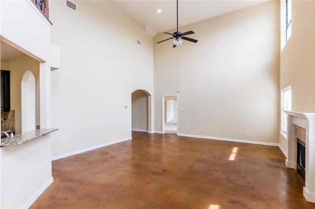 159 Catfish Cv, Dripping Springs, TX 78620 - unfurnished living room featuring arched walkways, a high ceiling, a ceiling fan, a fireplace, and concrete flooring