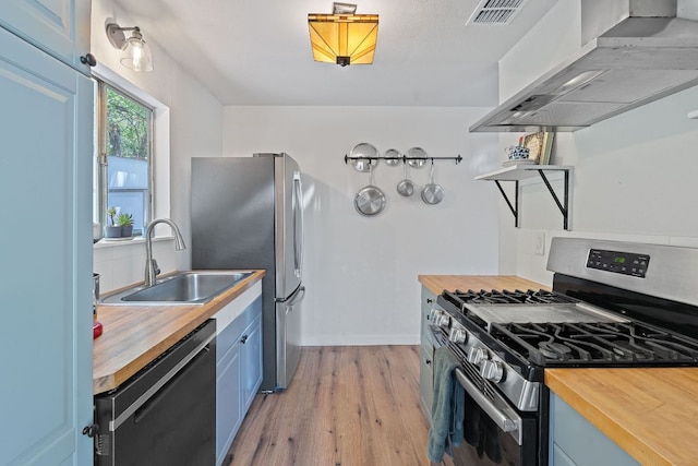 5206 Ledesma Rd, Austin, TX 78721 - kitchen featuring stainless steel appliances, wood counters, wall chimney exhaust hood, blue cabinetry, and light wood-style flooring