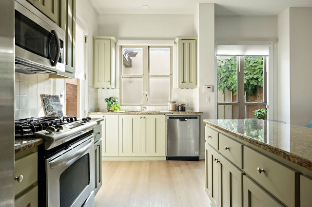 4048 Berkman Dr, Austin, TX 78723 - kitchen with appliances with stainless steel finishes, a sink, backsplash, light wood-style flooring, and dark stone countertops