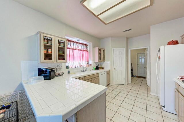 1610 Meadow Ln, Lockhart, TX 78644 - kitchen with white appliances, tile counters, a peninsula, tasteful backsplash, and glass insert cabinets