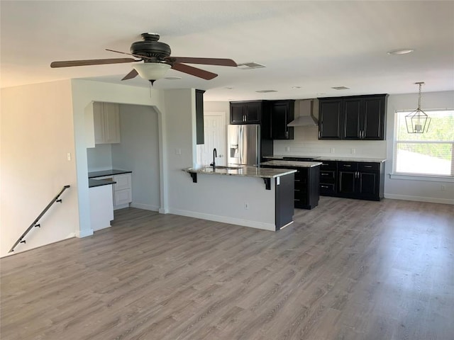 4102 Glendale Ln, Lago Vista, TX 78645 - kitchen featuring stainless steel fridge, wall chimney range hood, a kitchen breakfast bar, dark cabinets, and a peninsula