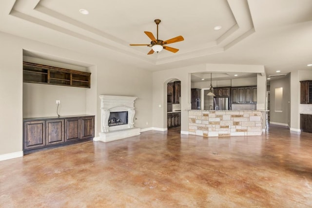 25036 River Rd, Spicewood, TX 78669 - unfurnished living room featuring a tray ceiling, finished concrete floors, baseboards, a fireplace with raised hearth, and recessed lighting
