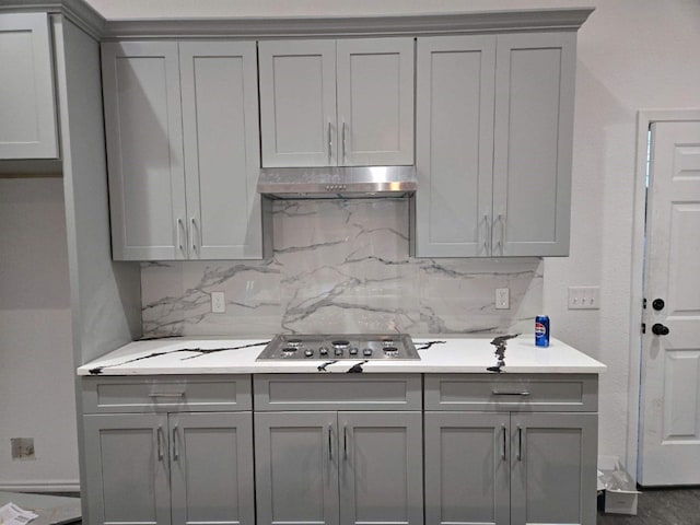 1525 Waco St, Gonzales, TX 78629 - kitchen featuring gray cabinetry, stainless steel cooktop, under cabinet range hood, decorative backsplash, and light countertops