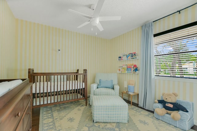 7000 Shadywood Dr, Austin, TX 78745 - bedroom with wallpapered walls, a textured ceiling, ceiling fan, wood finished floors, and a crib