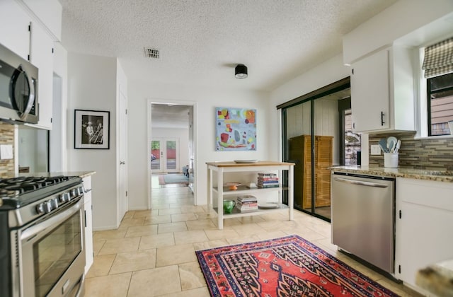 7000 Shadywood Dr, Austin, TX 78745 - kitchen with appliances with stainless steel finishes, backsplash, white cabinetry, healthy amount of natural light, and a textured ceiling