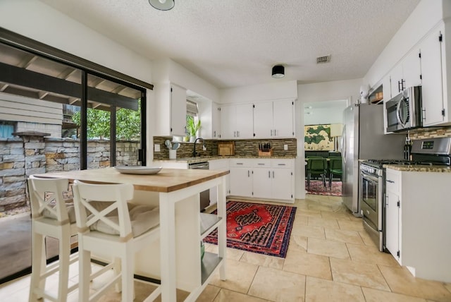 7000 Shadywood Dr, Austin, TX 78745 - kitchen featuring appliances with stainless steel finishes, backsplash, a textured ceiling, and white cabinets