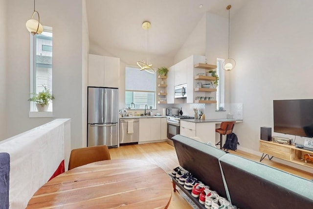 913 Duncan Ln Unit 103, Austin, TX 78705 - kitchen featuring stainless steel appliances, open shelves, light wood-style flooring, white cabinets, and high vaulted ceiling