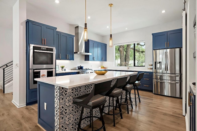 2312 Pruett St, Austin, TX 78703 - kitchen with stainless steel appliances, blue cabinetry, wall chimney range hood, a kitchen bar, and recessed lighting