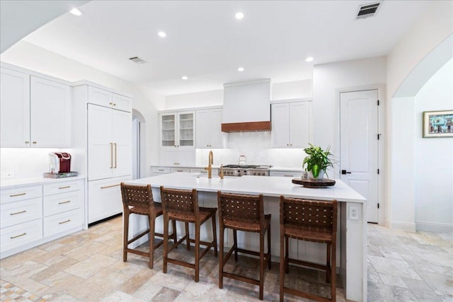 213 Black Wolf Run, Austin, TX 78738 - kitchen featuring custom range hood, arched walkways, stone tile floors, a kitchen bar, and light countertops