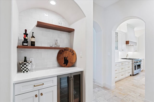 213 Black Wolf Run, Austin, TX 78738 - indoor dry bar featuring high end stainless steel range oven, wine cooler, custom range hood, backsplash, and light stone finish floors