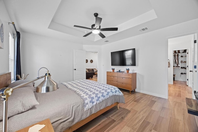 2545 Belle Hubbard Trl, Belton, TX 76513 - bedroom featuring a tray ceiling, light wood finished floors, ceiling fan, baseboards, and a walk in closet