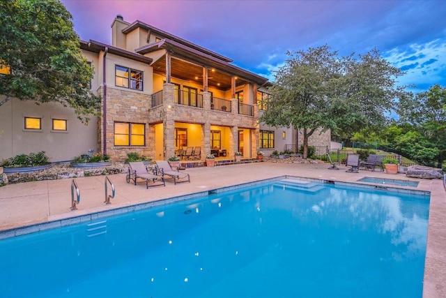1101 Sprague Ln, West Lake Hills, TX 78746 - back of house at dusk with a balcony, stone siding, a patio, and an outdoor pool
