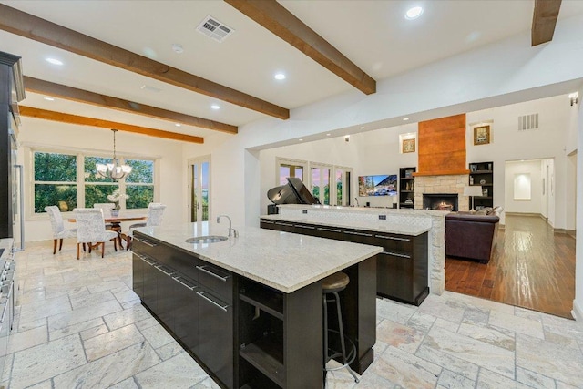1101 Sprague Ln, West Lake Hills, TX 78746 - kitchen featuring a kitchen island with sink, a sink, a fireplace, stone tile flooring, and beam ceiling