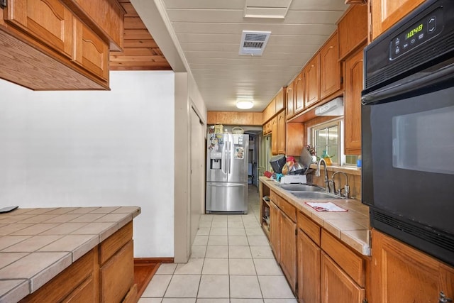 217 S Wilson St, San Marcos, TX 78666 - kitchen featuring tile counters, stainless steel fridge with ice dispenser, oven, light tile patterned flooring, and brown cabinetry