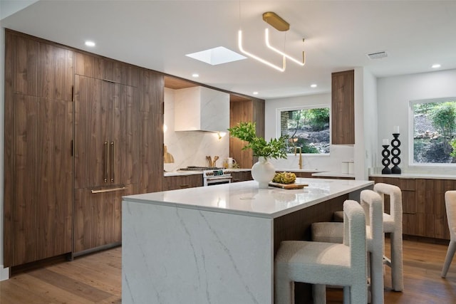 3403 Cascadera Dr, Austin, TX 78731 - kitchen featuring modern cabinets, a skylight, a kitchen breakfast bar, light wood-type flooring, and custom exhaust hood