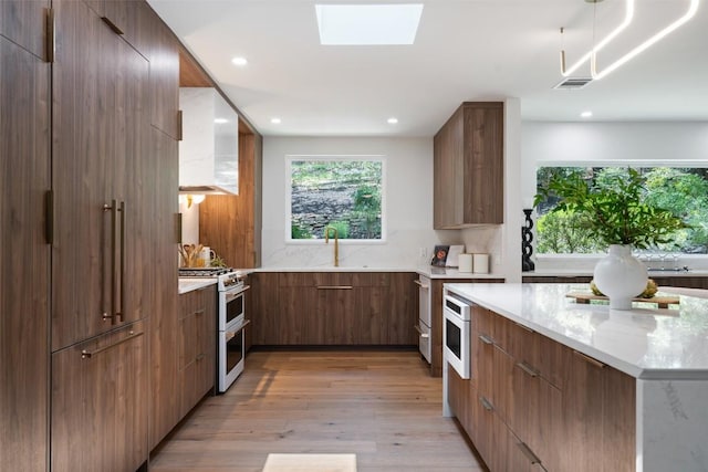 3403 Cascadera Dr, Austin, TX 78731 - kitchen with double oven range, modern cabinets, custom exhaust hood, light stone counters, and light wood finished floors